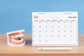 The April monthly desk calendar for 2024 year and model dentures on the table. Dental health concepts