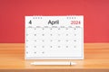 The April monthly desk calendar for 2024 year and pen on wooden table with red color background