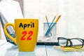 April 22nd. Day 22 of month, calendar on morning coffee cup, business office background, workplace with laptop and