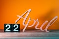 April 22nd. Day 22 of month, daily wooden calendar on table with orange background. Spring time concept