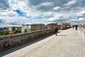 View of the street on the famous Roman Bridge of Ourense with people walking, the city behind and a cloudy blue sky above