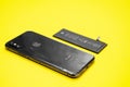 Broken iPhone of space grey color, lithium ion battery for mobile phone and portable devices are on yellow background