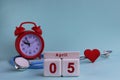 April 5st. White wooden calendar blocks with date, clock and stethoscope on a blue pastel background. Selective focus. health