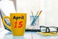 April 15th. Day 15 of month, calendar on morning coffee cup, business office background, workplace with laptop and