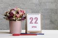 April 22. 22-th day of the month, calendar date.A delicate bouquet of flowers in a pink vase, two pencils and a calendar with a