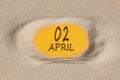 April 2. 2th day of the month, calendar date. Hole in sand. Yellow background is visible through hole