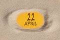 April 22. 22th day of the month, calendar date. Hole in sand. Yellow background is visible through hole