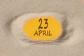 April 23. 23th day of the month, calendar date. Hole in sand. Yellow background is visible through hole