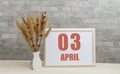 April 3. 3th day of month, calendar date. White vase with ikebana and photo frame with numbers on desktop, opposite