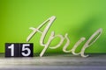 April 15th. Day 15 of month, calendar on wooden table and green background. Spring time, empty space for text