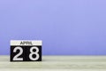 April 28th. Day 28 of month, calendar on wooden table and purple background. Spring time, empty space for text