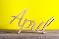 April - wooden carved word on yellow background. Spring time, 1st of april - Easter and fools day