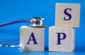 APS - acronym on wooden large cubes on blue background with stethoscope