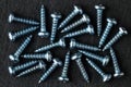 Aqua blue colored, stainless steel, pan head self-tapping screws on black stone surface. Top down, close up