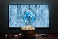 Aquaman and the Lost Kingdom trailer or movie on TV screen. TV with remote control and popcorn bowl.