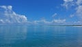 The aquamarine ocean is calm. There are picturesque cumulus clouds in the azure sky.