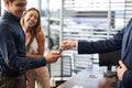 Ar salesman giving car keys to young woman sitting in car in auto dealership