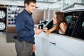 ar salesman giving car keys to young woman sitting in car in auto dealership