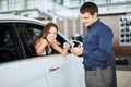 ar salesman giving car keys to young woman sitting in car in auto dealership