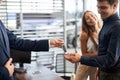 ar salesman giving car keys to young woman sitting in car in auto dealership