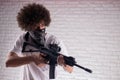 an Arab with an African hairstyle in stylish fashionable clothes with an airsoft gun poses against a brick wall