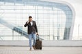 Arab businessman traveller talking on phone, while walking outside modern airport, carrying suitcase Royalty Free Stock Photo