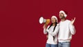 Arab Couple In Santa Hats Making Announcement With Loudspeaker Over Red Background Royalty Free Stock Photo