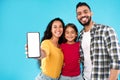 Arab Family Showing Cellphone Screen To Camera Over Blue Background