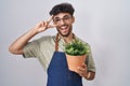 Arab man with beard holding green plant pot doing peace symbol with fingers over face, smiling cheerful showing victory Royalty Free Stock Photo