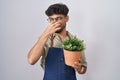 Arab man with beard holding green plant pot smelling something stinky and disgusting, intolerable smell, holding breath with