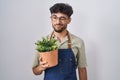 Arab man with beard holding green plant pot winking looking at the camera with sexy expression, cheerful and happy face