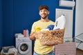 Arab man with beard holding laundry basket and detergent bottle winking looking at the camera with sexy expression, cheerful and