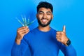 Arab man with beard holding picklock to unlock security door smiling happy and positive, thumb up doing excellent and approval