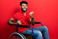 Arab man with beard sitting on wheelchair celebrating surprised and amazed for success with arms raised and eyes closed