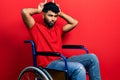 Arab man with beard sitting on wheelchair doing funny gesture with finger over head as bull horns