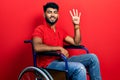 Arab man with beard sitting on wheelchair showing and pointing up with fingers number four while smiling confident and happy