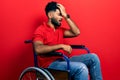 Arab man with beard sitting on wheelchair surprised with hand on head for mistake, remember error