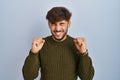 Arab man with beard standing over blue background excited for success with arms raised and eyes closed celebrating victory smiling Royalty Free Stock Photo