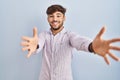 Arab man with beard standing over blue background looking at the camera smiling with open arms for hug Royalty Free Stock Photo