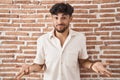 Arab man with beard standing over bricks wall background clueless and confused with open arms, no idea concept