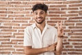 Arab man with beard standing over bricks wall background smiling with happy face winking at the camera doing victory sign with