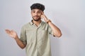 Arab man with beard standing over white background confused and annoyed with open palm showing copy space and pointing finger to