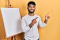 Arab man with beard standing by painter easel stand smiling and looking at the camera pointing with two hands and fingers to the Royalty Free Stock Photo