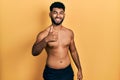 Arab man with beard wearing swimwear shirtless doing happy thumbs up gesture with hand