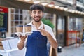 Arab man with beard wearing waiter apron at restaurant terrace smiling happy pointing with hand and finger