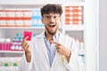 Arab man with beard working at pharmacy drugstore holding condom clueless and confused expression