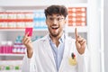 Arab man with beard working at pharmacy drugstore holding condom smiling and laughing hard out loud because funny crazy joke