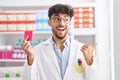 Arab man with beard working at pharmacy drugstore holding condom winking looking at the camera with sexy expression, cheerful and