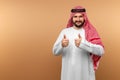 Arab man businessman in national clothes shows thumbs up, like, beige background. Dishdasha, kandora, thobe, middle east