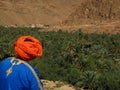 Arab man with orange turban and blue chilaba looks towards the palm grove in Morocco in October 2019